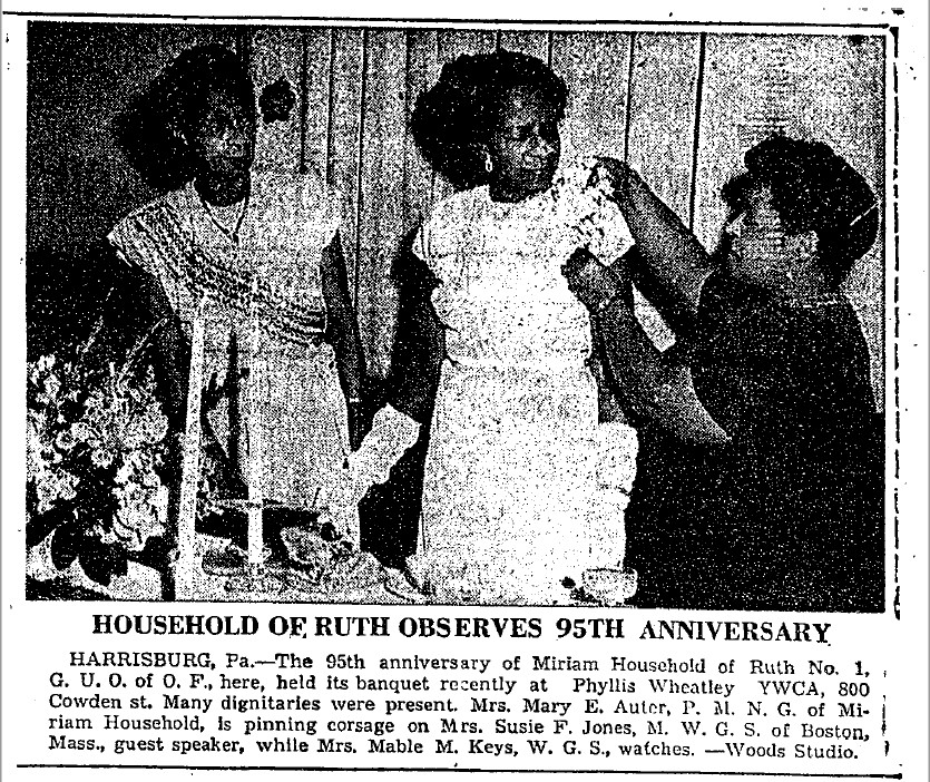 A newspaper clipping with a black and white photo of three black women. The one on the right is pinning a corsage on the one in the middle, while the woman on the left watches. The caption reads "household of Ruth observes ninety-fifth anniversary. Harrisburg, Pennsylvania. The ninety-fifth anniversary of Miriam Household of Ruth Number One, Great United Order of Odd Fellows here, held its banquet recently at Phyllis Wheatley YWCA, 800 Cowden Street. Many dignitaries were present. Mrs. Mary E. Auter, P.M.N.G. of Miriam Household, is pinning corsage on Mrs. Susie F. Jones, M.W.G.S. of Boston, Massachusetts, guest speaker, while Mrs. Mable. M. Keys, W.G.S., watches." 